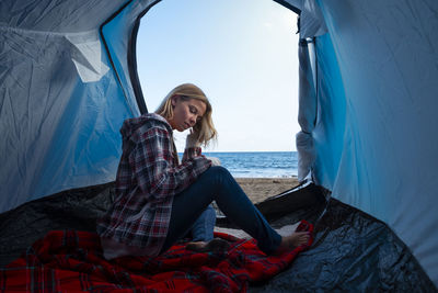 Woman sitting in tent at beach against sea and sky