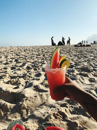 Cropped hand of person holding fruit juice on beach