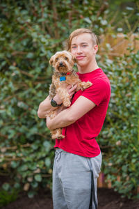 Portrait of smiling teenage boy with dog against plants