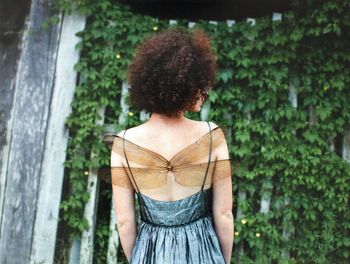 Rear view of woman with wings standing against plants