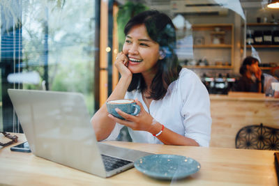 Smiling businesswoman drinking coffee while using technology in cafe