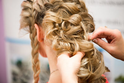 Close-up of female hairstylist holding blond customers hair at salon