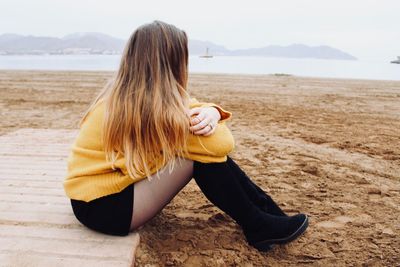 Young woman sitting at beach against sky