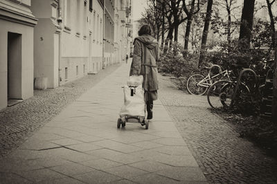 Rear view of woman walking on footpath with luggage cart