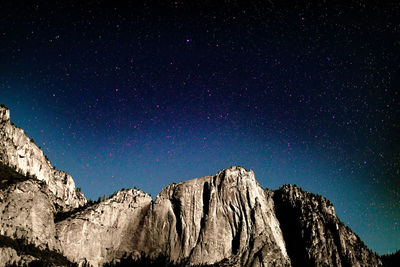 Low angle view of rocky mountains against starry sky