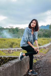 Portrait of young woman standing on field against sky