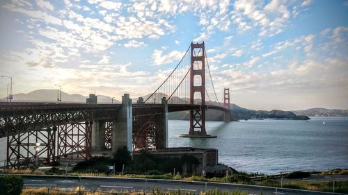 Suspension bridge over river against cloudy sky