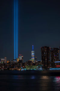 Illuminated buildings by river against sky at night
