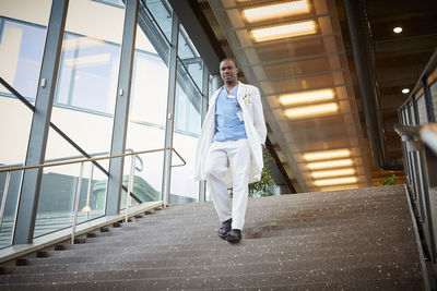 Low angle view of confident male doctor moving down on staircase at hospital