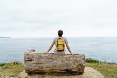 Rear view of woman standing on rock by sea against sky