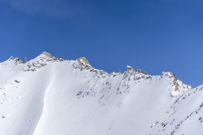 Low angle view of snowcapped mountains against clear blue sky
