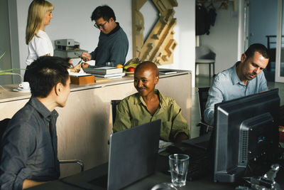 Multiracial male and female business professionals working while sitting at desk in office