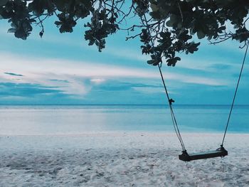 Swing hanging over sea against sky