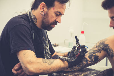 Artist making tattoo on shirtless man shoulder