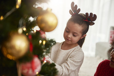 Girl by mother decorating christmas tree