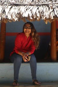 Portrait of smiling young woman sitting on wall