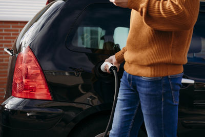 Man holding electric plug and charging car at electric vehicle charging station