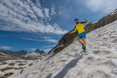 Skyrunner man run downhill on snow between sky and mountains