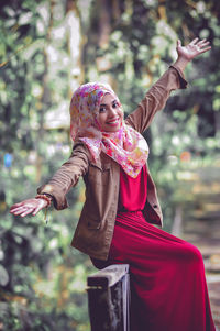 Portrait of smiling woman with arms raised standing outdoors