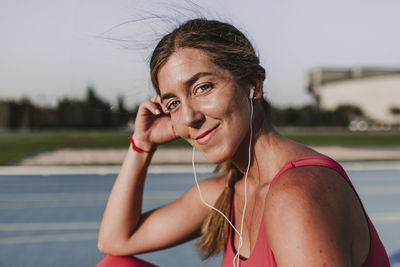 Portrait of female athlete listening music while sitting on sports track