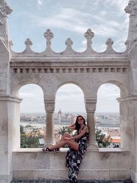 Full length of woman sitting with hungarian parliament building in background