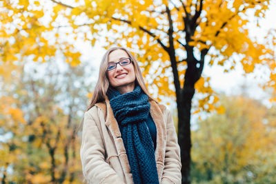 Portrait of smiling young woman standing against trees during autumn