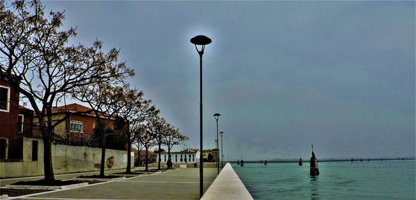 Street light by sea against sky in city