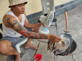 A man is sitting and grilling fish