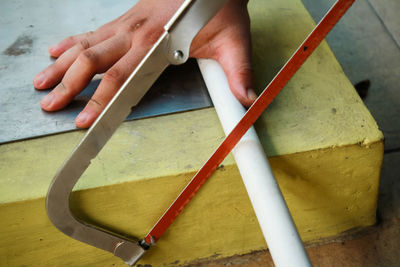 Cropped hands of man cutting pipe with hand saw