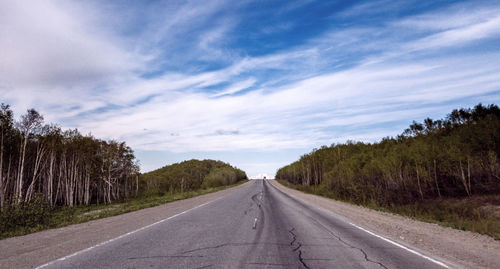 Empty road along trees and against sky