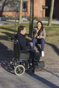 Young woman and man on wheelchair having coffee break