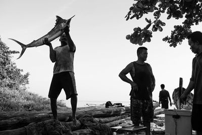 People standing by tree against clear sky