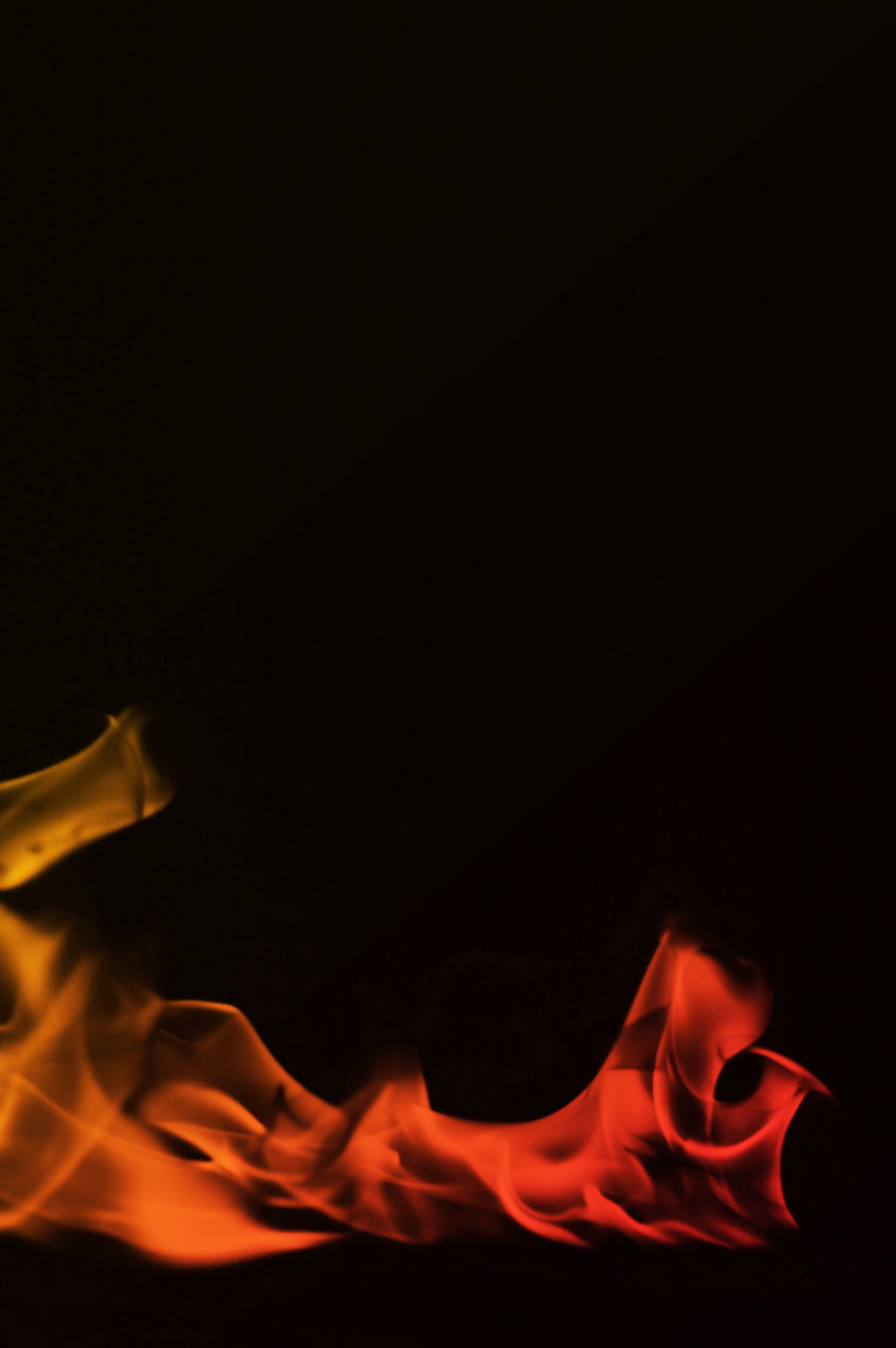 CLOSE-UP OF LIT CANDLE AGAINST BLACK BACKGROUND