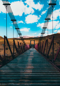 Diminishing perspective of empty bridge leading towards mountain against sky