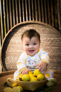 Portrait of cute baby boy holding lemons sitting on wicker seat