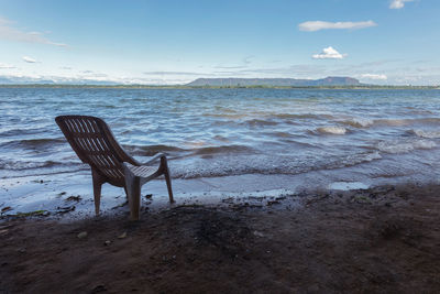 Chair on beach by sea against sky