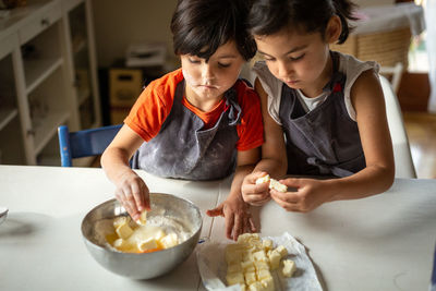 Two girls wearing grey aprons adding butter to flour