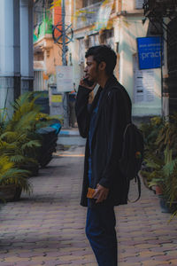 Young man looking away on footpath in city