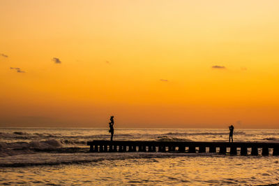 Silhouette people standing on beach against orange sky