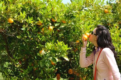 Woman smelling oranges while standing against plants