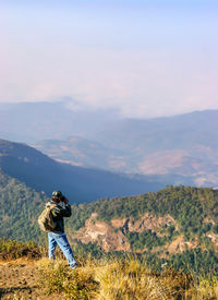 Rear view of man photographing on mountain against sky