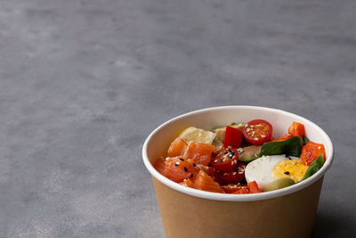 Takeaway poke bowl with  salmon, avocado, quinoa and vegetables in recycled kraft paper packaging. 