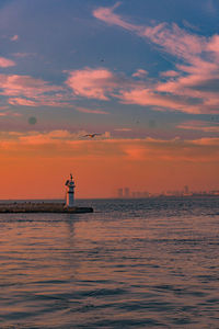 Lighthouse by sea against sky during sunset