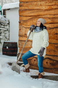 Smiling young woman standing on snow field by cottage