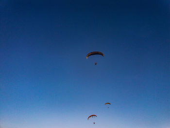 Low angle view of people paragliding against clear blue sky