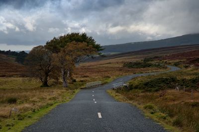 Road amidst field against cloudy sky