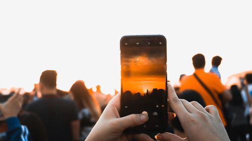 Cropped hand photographing sunset through mobile phone