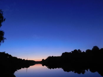 Reflection of silhouette trees in lake against clear sky