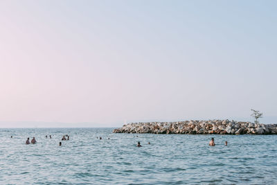 People swimming in sea against clear sky