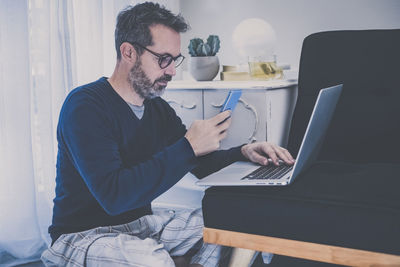 Man works with laptop sitting on the sofa.  boy shopping online with computer, pad and smartphone. 